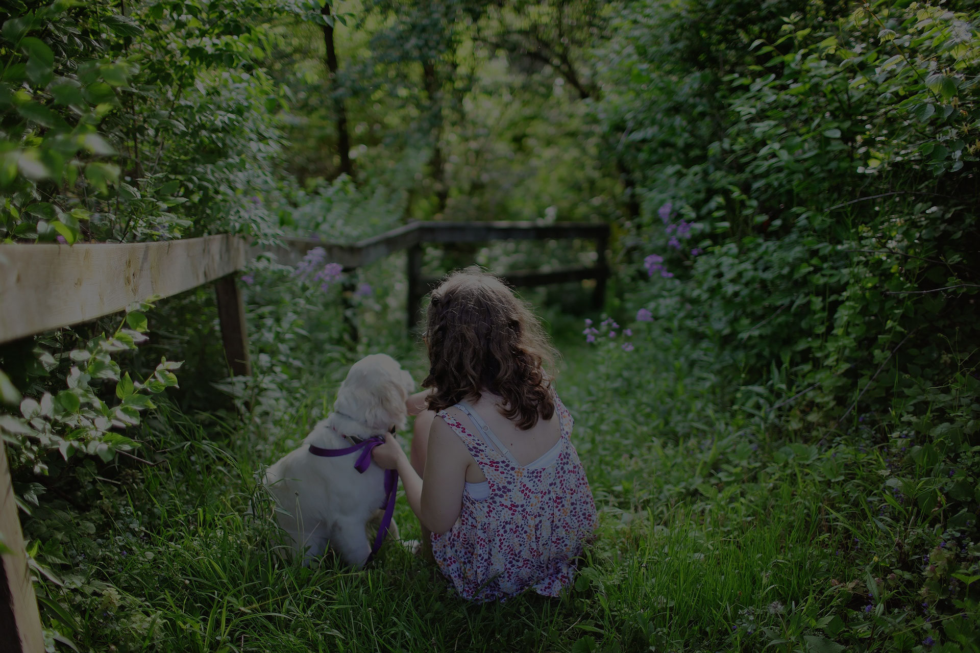 girl-and-puppy-sitting-on-green-grass-surrounded-with-shrubs-during-daytime
